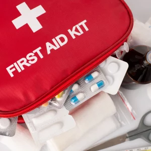 Close-up of an open red first aid kit with visible medical supplies including blister packs of pills, gauze, scissors, and a medicine bottle.