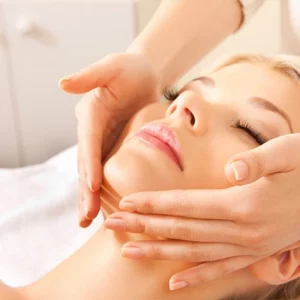 Woman lying down with eyes closed receiving a gentle facial massage from a professional, suggesting a relaxing skincare or spa treatment.