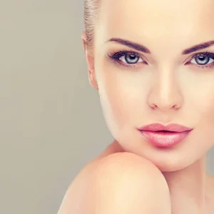 Portrait of a woman with flawless, glowing skin, enhanced makeup, and a soft expression, showcasing beauty and skincare results against a neutral background.