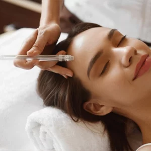 Woman receiving a relaxing facial treatment with a microdermabrasion or vacuum-based skincare device while lying on a spa bed, smiling with eyes closed.