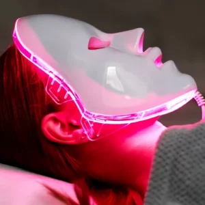 Person lying down wearing a white LED light therapy mask emitting red light, used for skin rejuvenation and facial treatment.