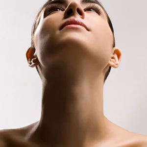 Close-up image of a woman tilting her head back, showcasing a smooth, well-defined neck and jawline against a neutral background.
