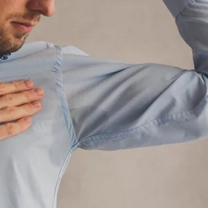 Man checking excessive underarm sweating, visible through a large sweat stain on his light blue shirt.