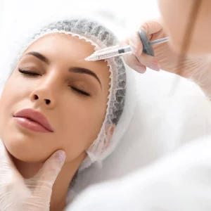 Close-up of a woman receiving a cosmetic injection in her forehead by a medical professional wearing gloves and a protective cap, during a beauty or aesthetic treatment.