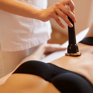 Close-up of a woman receiving a non-invasive body contouring treatment on her abdomen using a handheld ultrasound or radiofrequency device in a clinical or spa setting.