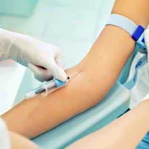 Medical professional wearing white gloves drawing blood from a patient's arm using a syringe and a tourniquet, in a clinical or laboratory setting.