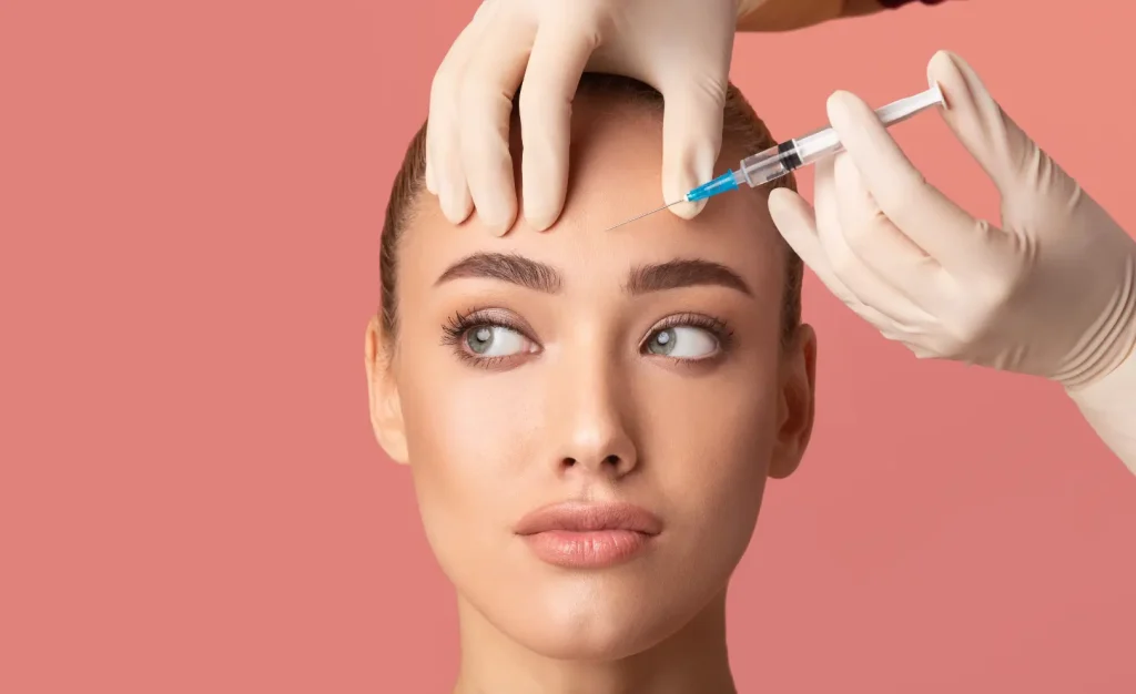 Gloved hands hold a syringe near a woman's forehead while stabilizing the skin above her eyebrows.