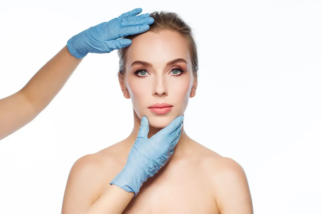 Gloved practitioner positions hands near a woman's forehead and jaw during a facial assessment.