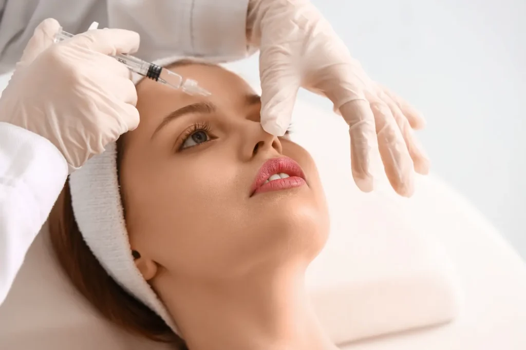 Gloved practitioner positions a syringe near a woman's forehead while supporting the treatment area.